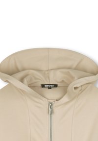 Beige hoodie met een volledige rits, gemaakt van zacht materiaal, met een gladde textuur en een DKNY-label aan de binnenkant van de nek.