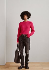 Rode gebreide trui met ribbelstructuur, hoge hals, zwarte Hoge taille jeans, chunky zwarte schoenen en een zwarte tote bag.