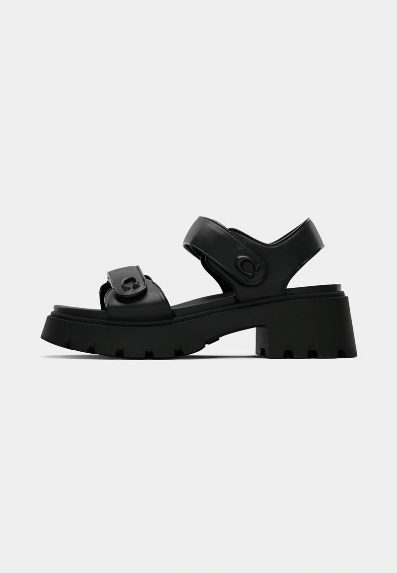 Sandalias de plataforma negras con suelas de goma gruesas y texturizadas, correas ajustables y un upper de cuero suave con un acento de logo circular.