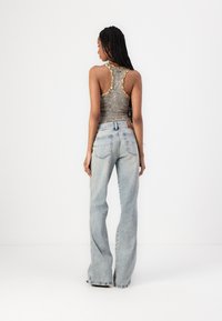 Top gris sin mangas con bordes ondulados, combinado con unos vaqueros acampanados de color azul claro. Los vaqueros tienen bolsillos traseros y una etiqueta de la marca en la cinturilla.