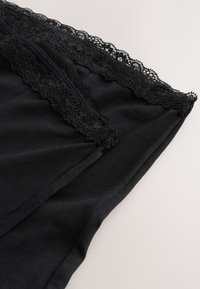 Gros plan d'un vêtement en tissu noir avec une bordure en dentelle noire complexe le long du bord, mettant en valeur la texture et les détails.