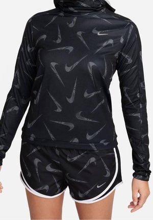 Ensemble sportif noir composé d'un haut à manches longues et d'un short avec des logos blancs Nike Swoosh répétés, porté par une personne sur un fond uni.
