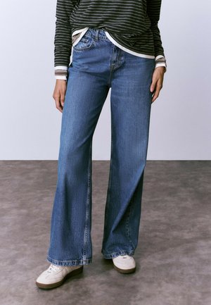 Jeans de mezclilla de tiro alto y pierna ancha color azul claro, con costuras visibles, bolsillos laterales y un ajuste relajado con dobladillos deshilachados.