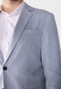 Hellblauer Blazer mit feinen Streifen, einreihiger Knopfleiste, Reverskragen und einer Brusttasche. Der Stoff wirkt strukturiert und maßgeschneidert.