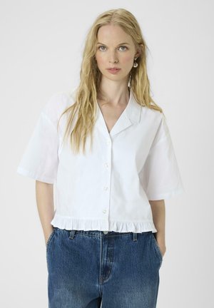 White short-sleeve button-up shirt with a collar and ruffled hem. Paired with high-waisted blue denim jeans. Smooth fabric texture.