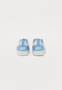 Baskets Nike présentant une combinaison de matériaux bleu clair et blancs. Le design inclut un logo blanc sur le talon et des accents texturés.