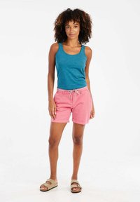 Turquoise tanktop gecombineerd met roze shorts met een trekkoord in de taille en een gepatternde accenten. Het model draagt beige sandalen.