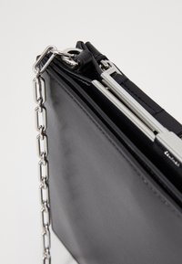 Bolsa de couro preto com uma alça de corrente prateada, apresentando um design estruturado e um mecanismo de abertura elegante. Superfície texturizada com acabamento mate.