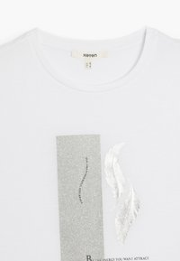 Hvid kortærmet T-shirt med glitrende sølvgrafik, der har tekst og bladmotiver, rund halsudskæring og blødt bomuldsstof.