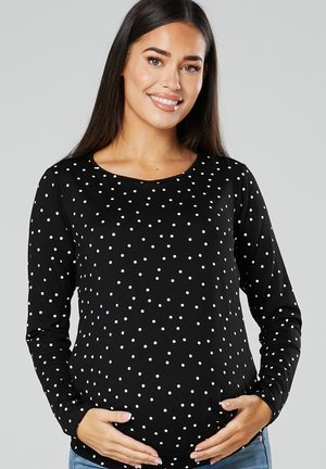 Black long-sleeve shirt with white polka dots, round neckline, fitted design, stretch fabric, worn over a rounded belly, paired with blue jeans.