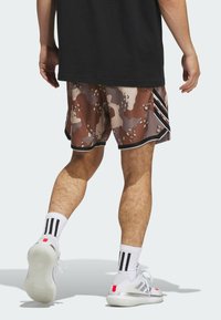 Brune og beige camouflageshorts med sort kant og tre striber på siden. Sammen med hvide sko og sort-hvide stribede sokker.