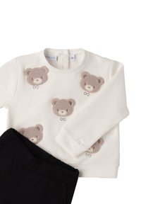 Biała bluza z aplikacjami w kształcie beżowego misia, okrągły dekolt i długie rękawy, w połączeniu z czarnymi spodniami z elastycznym paskiem.