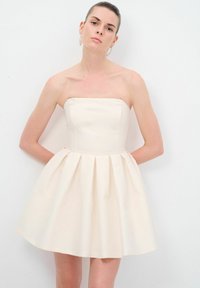 Robe crème sans bretelles avec un corsage ajusté, une jupe plissée évasée et un tissu à texture lisse, adaptée aux occasions formelles.