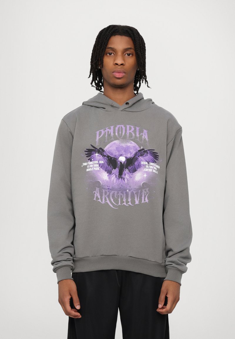 Felpa grigia con cappuccio caratterizzata da un design grafico con testo viola e un'illustrazione di un'aquila contro una luna, maniche lunghe e cappuccio con cordoncino.