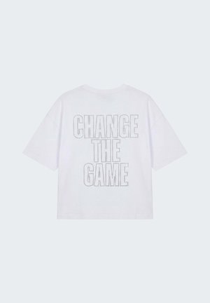 Camiseta blanca de manga corta con el texto "CHANGE THE GAME" en contorno punteado en la parte trasera, exhibida sobre un fondo claro y liso.