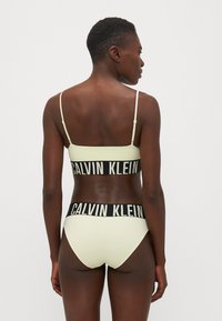 Lichtgele bikini set met een bralette met verstelbare bandjes en hooggekraagde onderkant, verfraaid met een zwarte Calvin Klein logo-band.