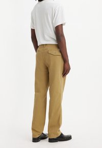 Khaki bomullsbukser med rak bendesign, med bakfickor, en liten logotagg och en mjuk textur. Bärs med en vit t-shirt.