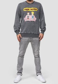 Sweat-shirt gris avec un graphisme de personnages animés, col rond et poignets côtelés. Assorti à un jean gris clair et des baskets blanches.