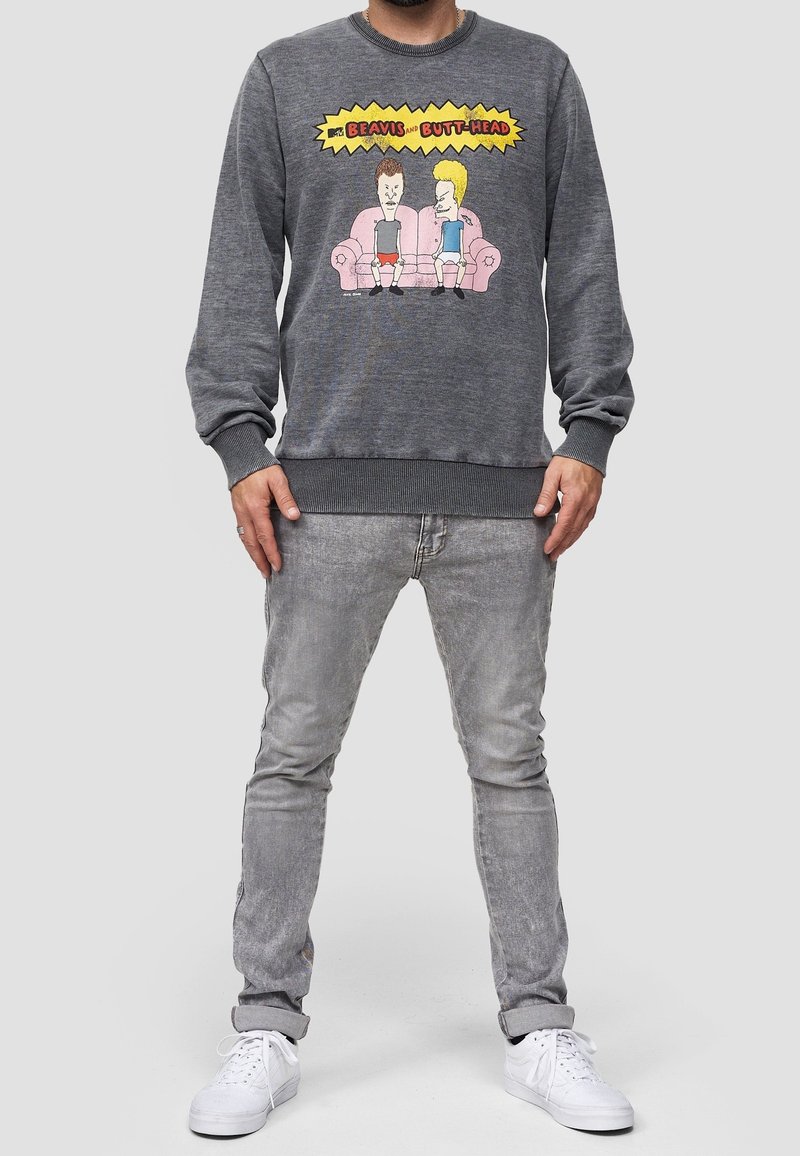 Sweat-shirt gris avec un graphisme de personnages animés, col rond et poignets côtelés. Assorti à un jean gris clair et des baskets blanches.