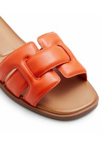 Tongs en cuir orange avec un design à large bandage aux panneaux texturés et une semelle plate tan.