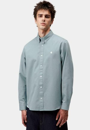 Camisa de manga larga azul claro, de botones y hecha de algodón, que presenta un cuello clásico, botones blancos y un pequeño logo en el pecho.