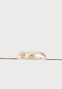 Reloj de pulsera en oro rosa con bisel engastado en diamantes, correa de cuero blanca y corona lateral, mostrado en perfil lateral sobre fondo blanco.