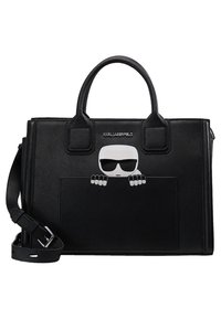 Mustavärinen muotolaukku, jossa on yläkahvat ja olkahihna. Laukussa on ulkopuolella tasku, jossa on piirretty hahmo aurinkolaseissa kurkistamassa taskun yli.