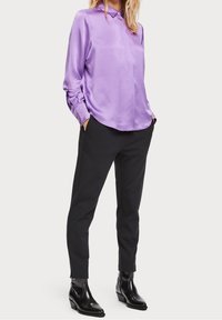 Blusa di raso lavanda con colletto e chiusura a bottoni, abbinata a pantaloni neri aderenti e stivaletti neri lucidi.