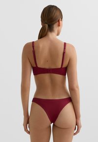 Burgundské bikini s texturovaným designem, nastavitelnými ramínky a zapínáním na sponu. Spodní díl má střih s vysokým vystřižením nohou.