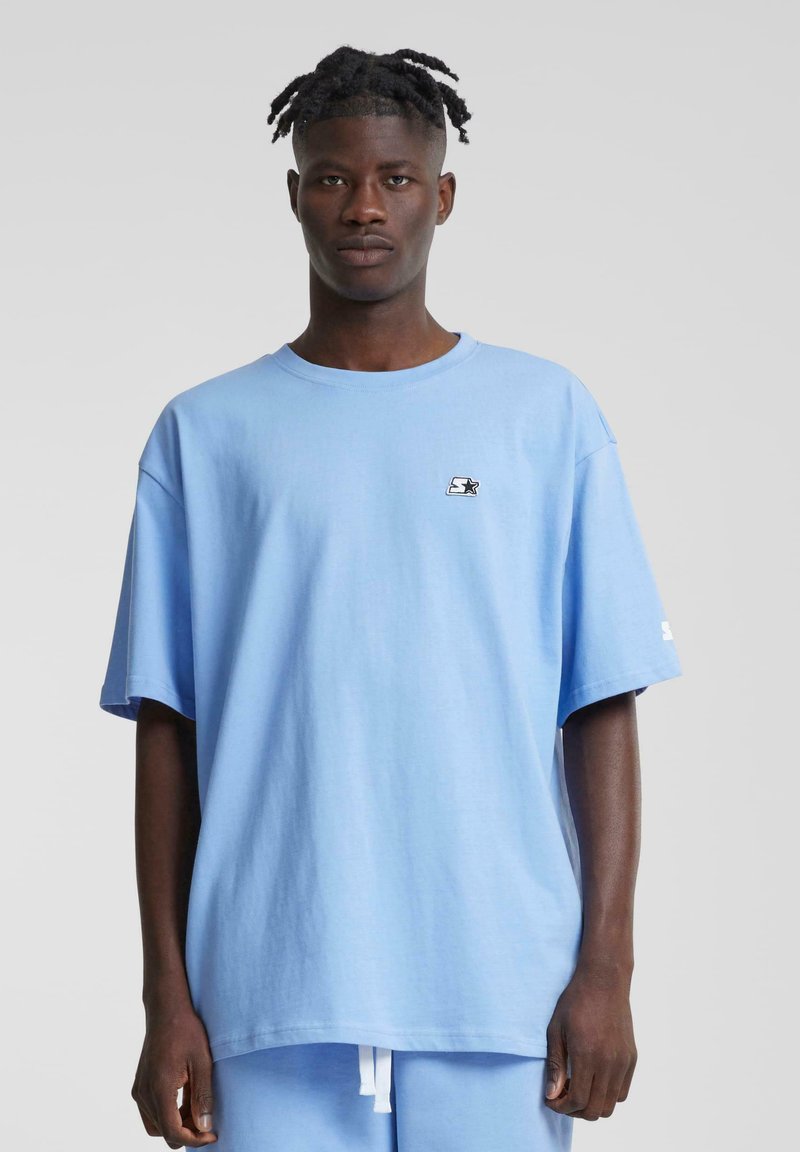 T-shirt en coton surdimensionnée de couleur bleu clair avec un petit logo noir sur la poitrine et des manches courtes, assortie à un short bleu clair.