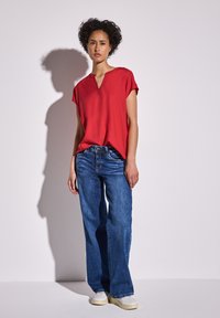Top rosso con maniche corte e scollatura a V, abbinato a jeans in denim blu larghi e sneakers bianche. Design semplice e casual con una vestibilità comoda.