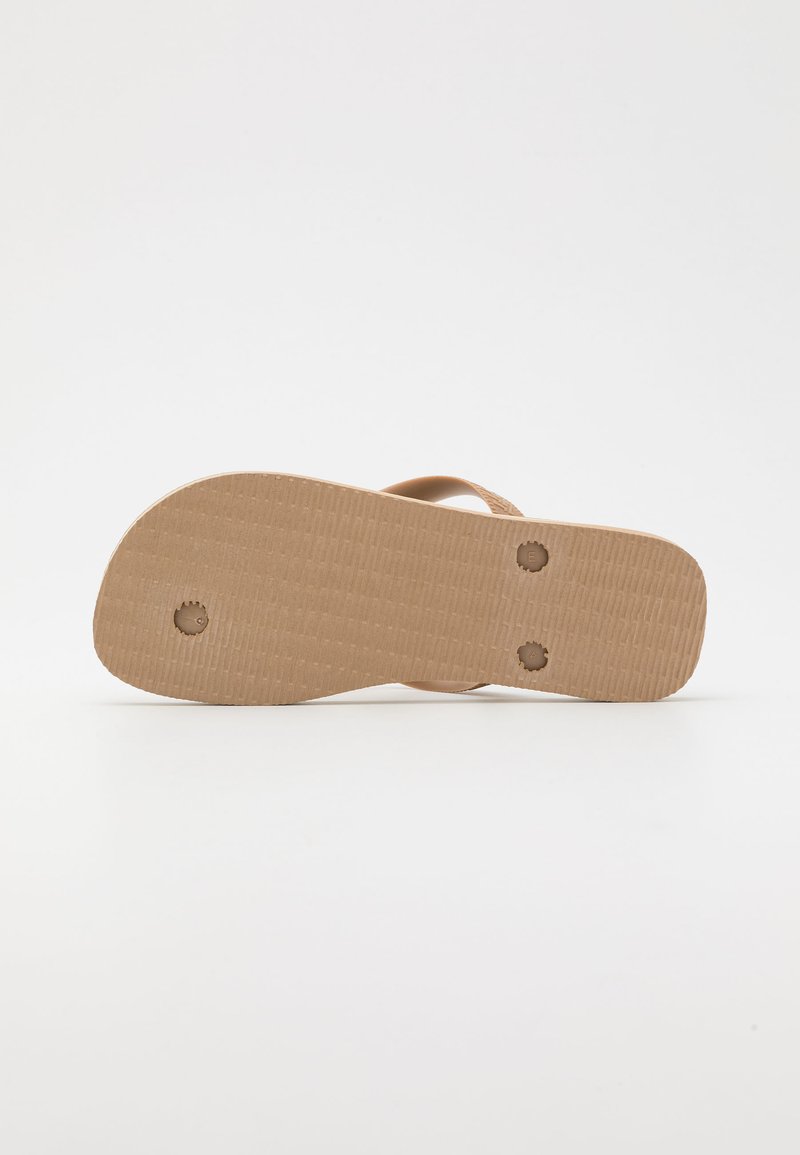 Semelle de tongs en caoutchouc beige avec une surface texturée et deux rainures circulaires. Design minimaliste avec un profil plat et sans embellissements supplémentaires.