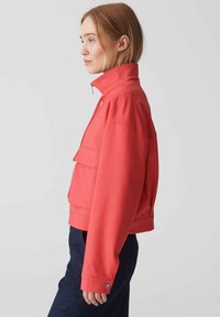 Rote Zip-Jacke mit hohem Kragen, überschnittenen Schultern und zwei vorderen Taschen. Hergestellt aus glattem Stoff mit einer lockeren Silhouette.