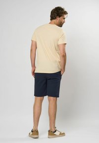 Tricou bej cu mânecă scurtă și pantaloni șort bleumarin. Adidași maronii cu accente albe. Textură din țesătură naturală. Design curat, minimalist.