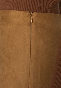 Brun ruskind med et ribbet brunt strikdesign øverst. Har en sidelukning med lynlås for lukning, der blander teksturer og farver.