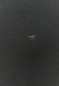 Černá texturovaná tkanina s jemným tkaným vzorem, vybavená malým vyšívaným hnědým logem koně v levém horním rohu.