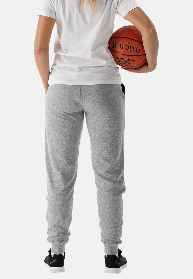 Grijze joggingbroek met een elastische tailleband en boorden, zakken aan de zijkanten, gecombineerd met een wit T-shirt en zwarte sportieve schoenen.