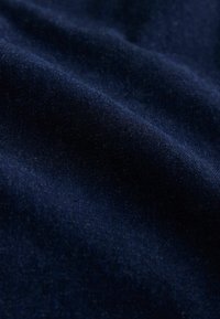 Tamsiai mėlynas aksomo audinys su švelnia, lygiomis tekstūra ir šiek tiek blizgesio, rodantis švelnius raukšles ir šviesą, atspindinčią paviršių.