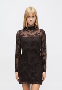 Robe noire avec manches longues en tulle, broderie florale, col montant et silhouette ajustée, fabriquée en tissu léger.