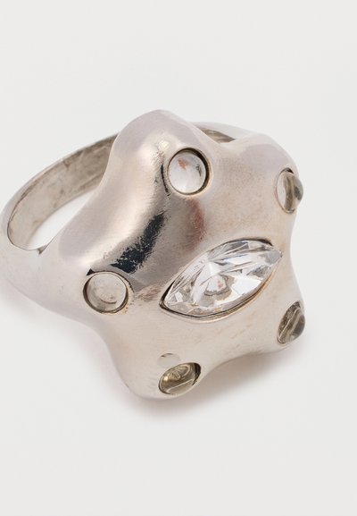 Zilveren ring met een organische vorm, voorzien van een centrale heldere edelsteen en meerdere kleinere heldere stenen die rond de ringband zijn geïnmeerd.