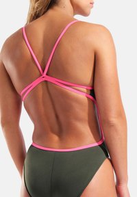 Tył osoby ubranej w ciemny kostium kąpielowy z różowymi ramionkami krzyżującymi się na górnej części pleców i obrysowującymi krawędzie.