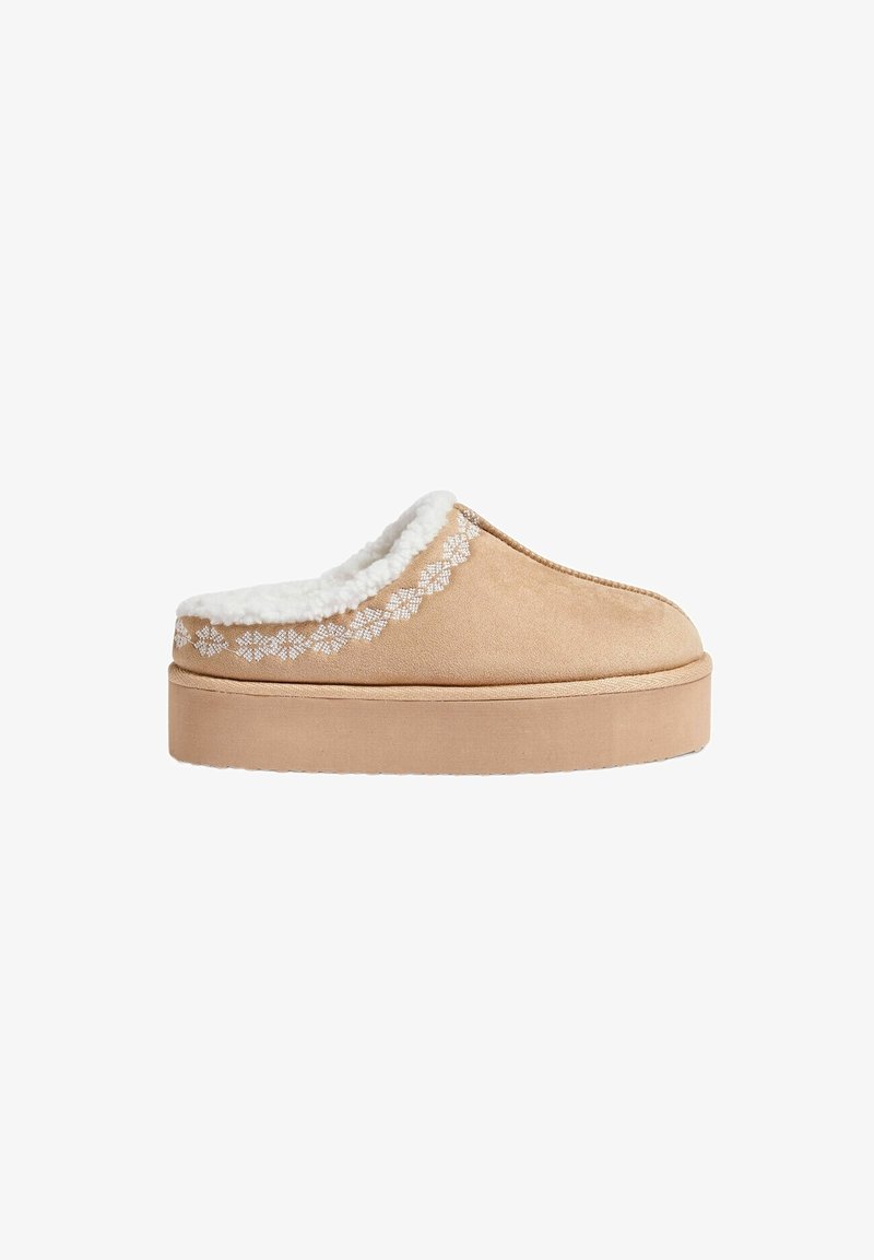 Chausson beige en daim à enfiler avec une semelle épaisse, une doublure en polaire blanche et des coutures décoratives blanches près du col de la cheville.