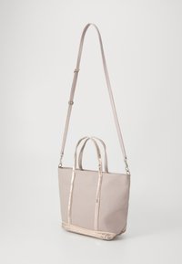 Canvas tygväska i mjukt beige med två övre handtag och en justerbar axelrem. Har glänsande metalliska detaljer längs sömmarna.