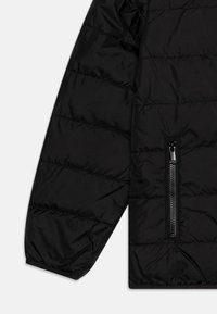 Manga de una chaqueta negra acolchada con costuras horizontales y un bolsillo con cremallera vertical cerca del puño.