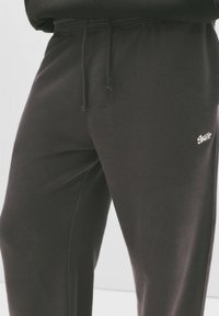 Donkergrijze sweatpants van zacht materiaal, met een elastische tailleband met een trekkoord en een klein wit logo op de linker dij.