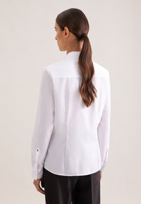 White long-sleeve shirt with a tailored fit, a classic collar, and buttoned cuffs. Smooth fabric with a subtle sheen, no visible patterns.