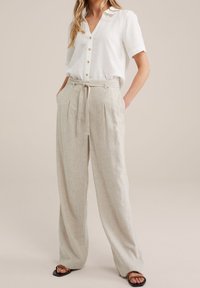 Lätta, beige veckade byxor med hög midja, tygbälte och sidofickor; parat med en vit skjorta med knappar.