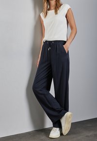 Top bianco senza maniche abbinato a pantaloni larghi blu navy con vita elastica e tasche laterali, completato da sneakers bianche.
