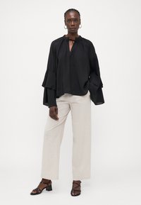 Black, loose-fitting blouse with long, ruffled sleeves and a tie neckline, paired with light beige wide-leg pants and black strappy sandals.