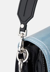 Dettaglio di una borsa in pelle azzurro chiaro con attacco per tracolla in gomma nera, hardware in argento e cuciture bianche a contrasto.